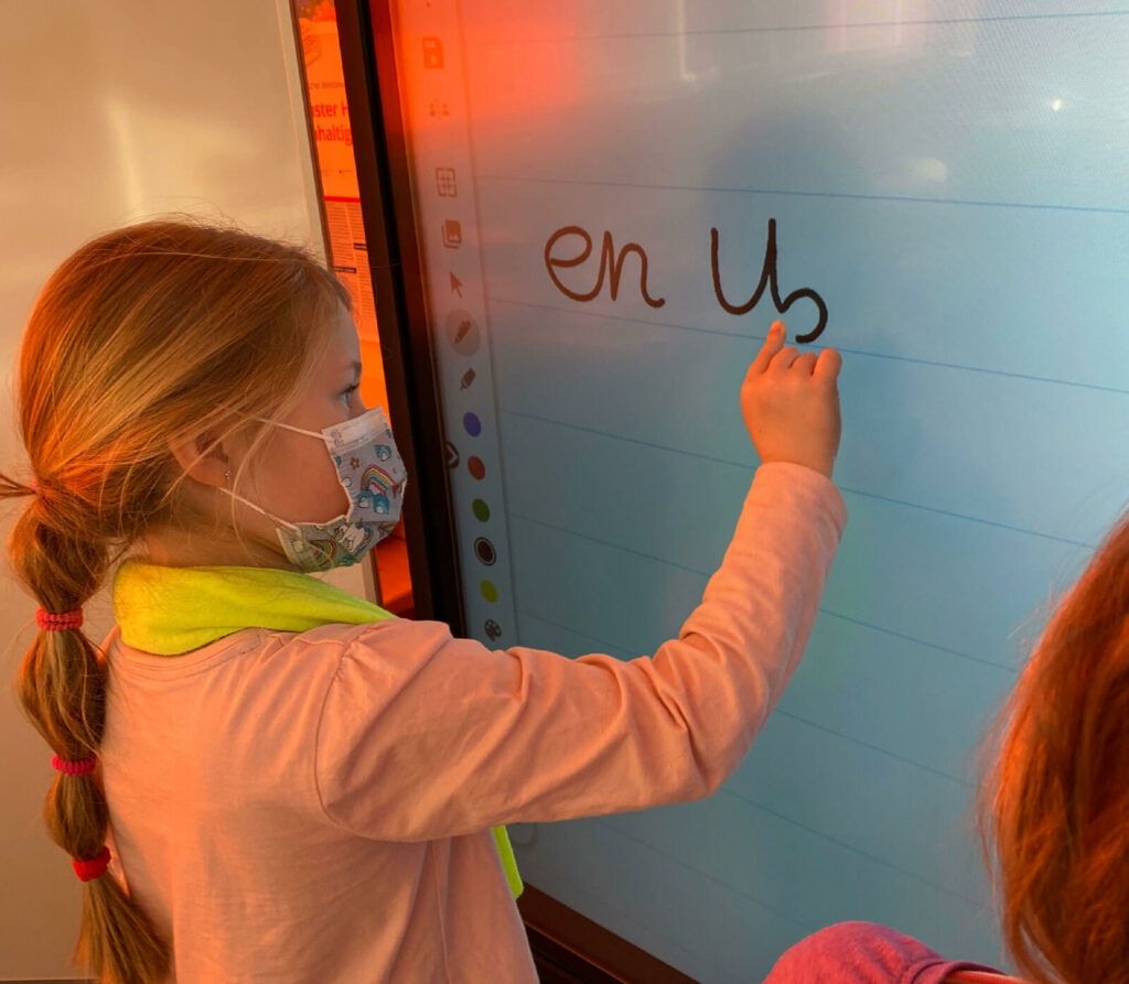 Kleines Mädchen schreibt mit ihrem Finger an einem Touchscreen-Monitor in der Schule.