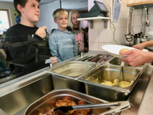 Drei Schulkinder stehen in der Schulküche an und entscheiden was sie essen möchten.